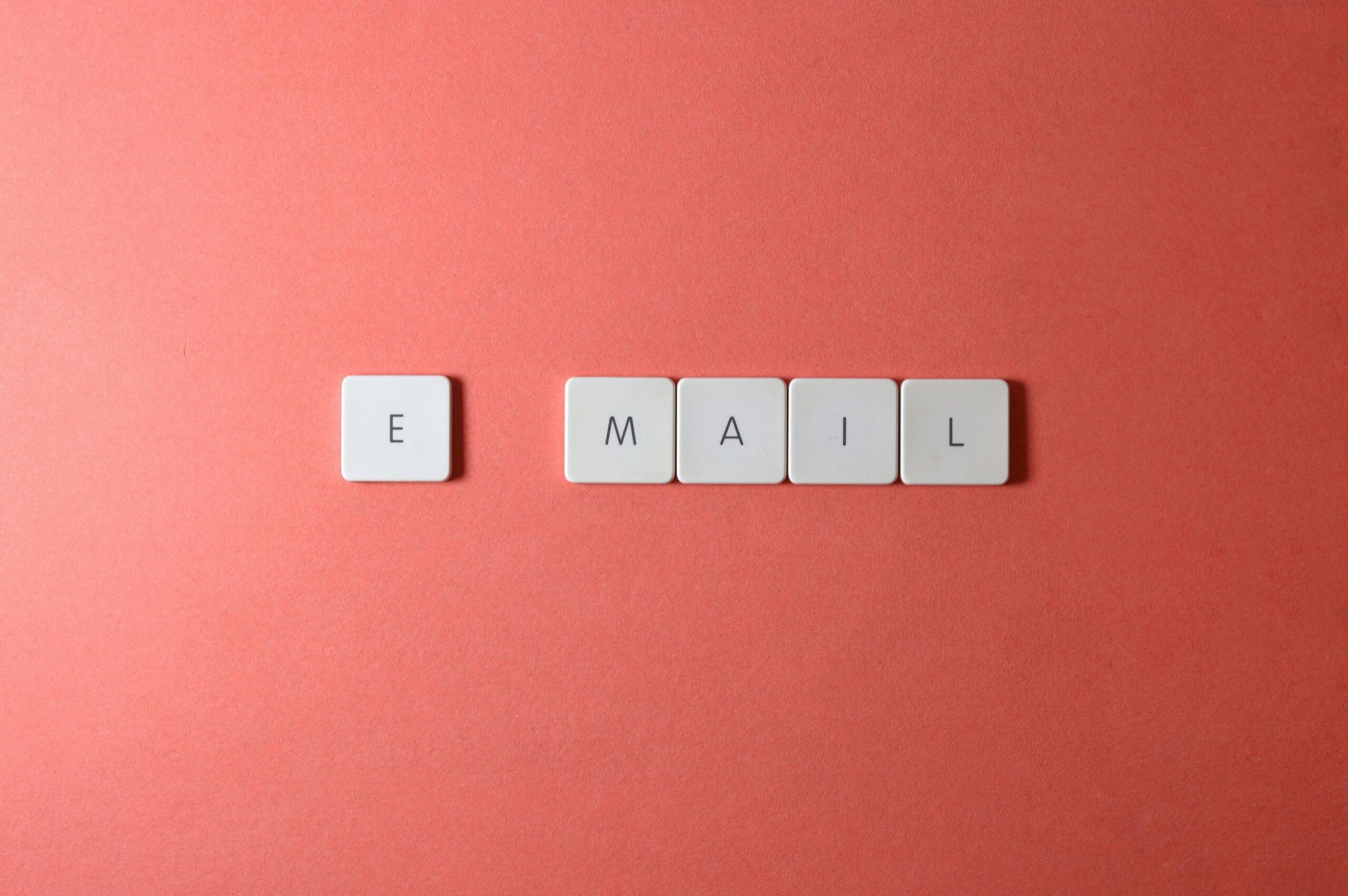 Flat lay of keyboard letter tiles spelling 'email' on coral backdrop.