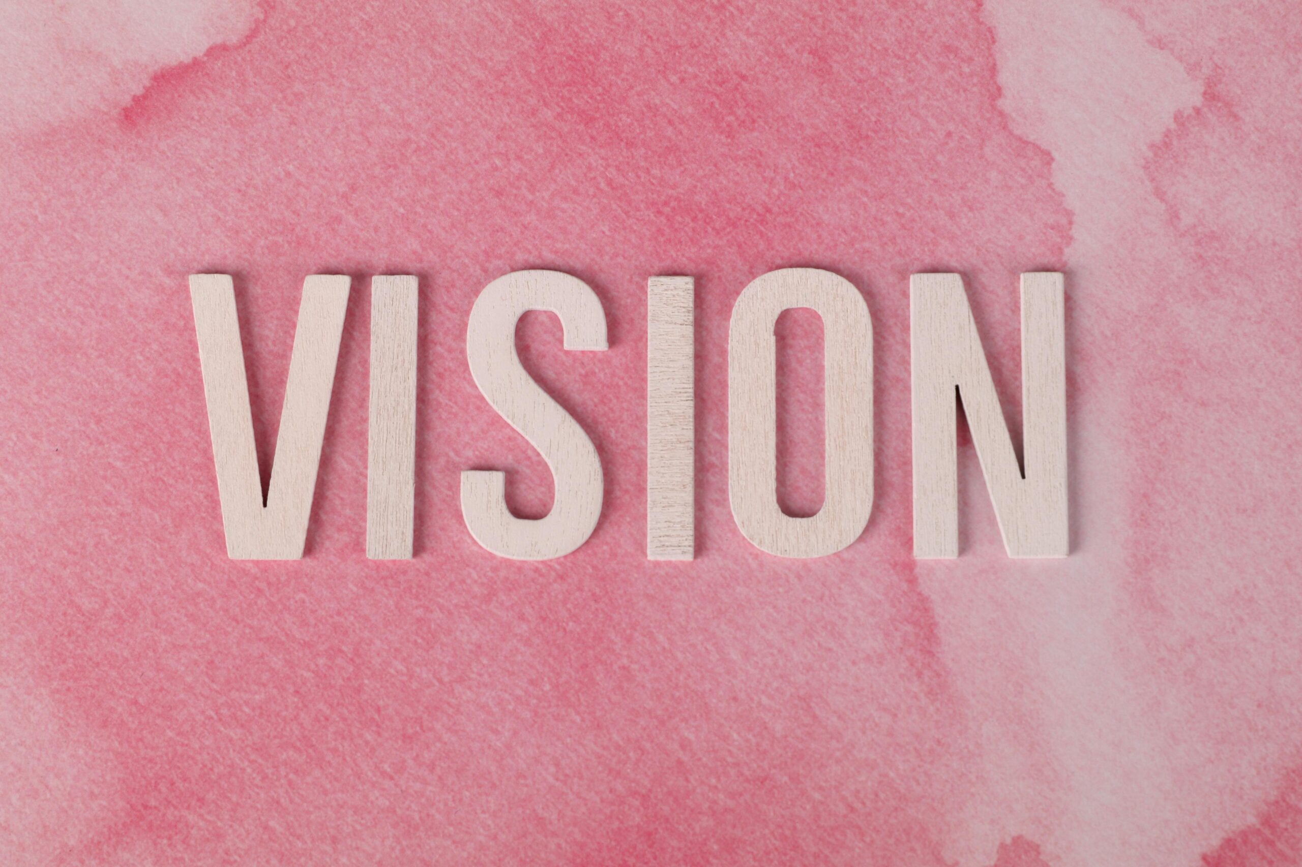 Wooden letters spelling 'VISION' on a textured pink watercolor background.