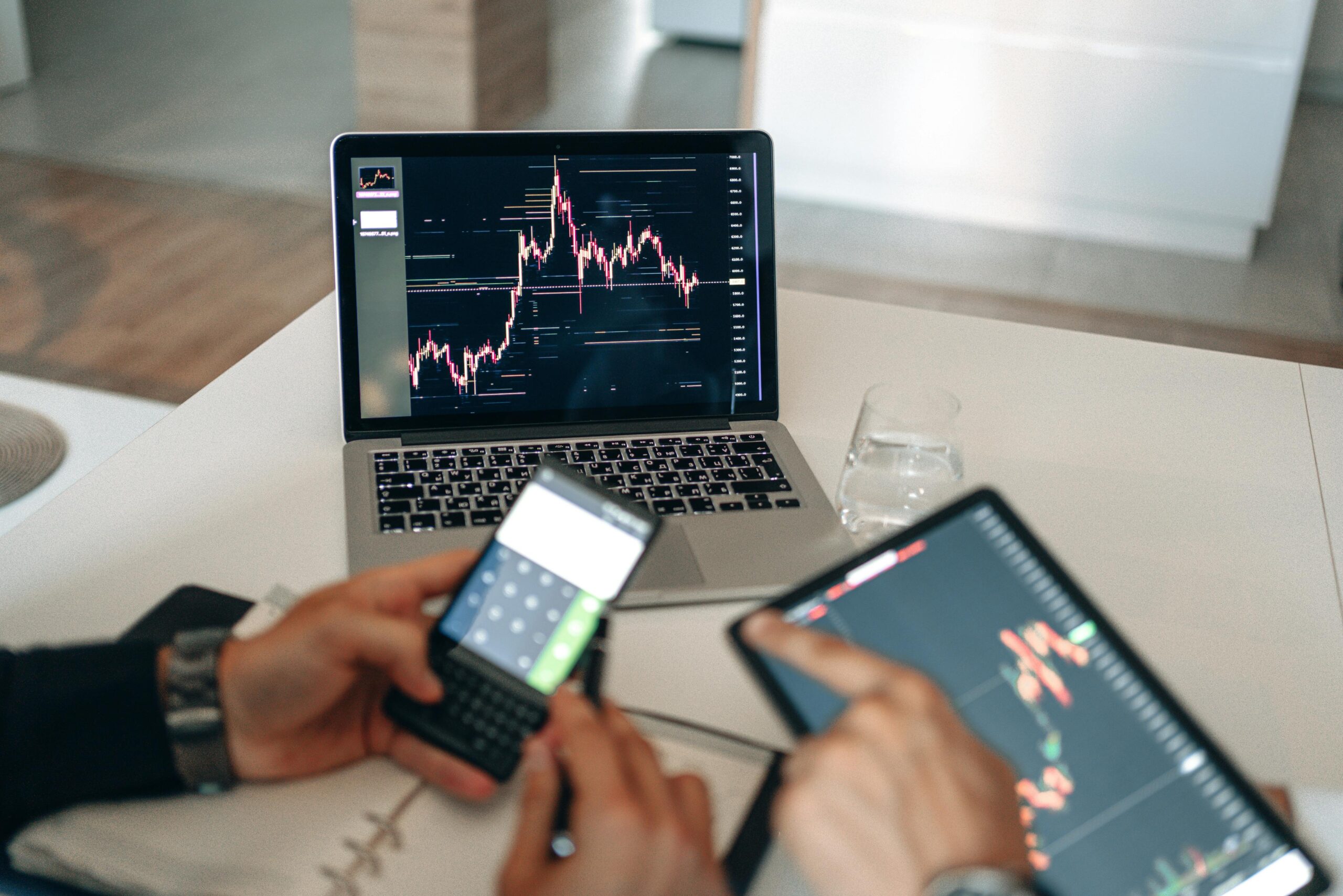 Hands using digital devices for financial analysis at a modern desk setup.