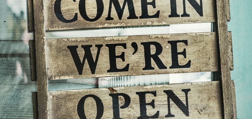Rustic wooden sign on a turquoise door reading 'Come In We're Open'.