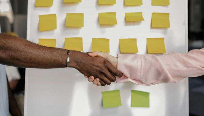 Colleagues shaking hands in front of a marketing board during a business meeting.